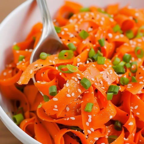 A bowl of pasta with orange carrots and green peppers.