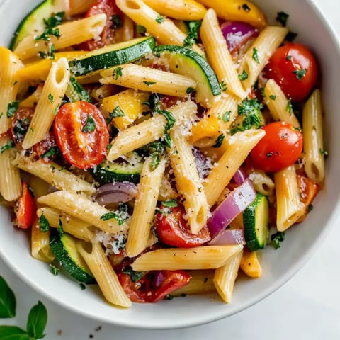 A bowl of pasta with tomatoes, zucchini, and basil.